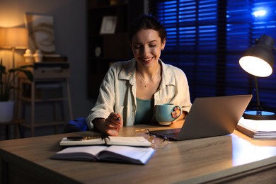 Photo of Woman with cup of coffee working on laptop at desk in home office