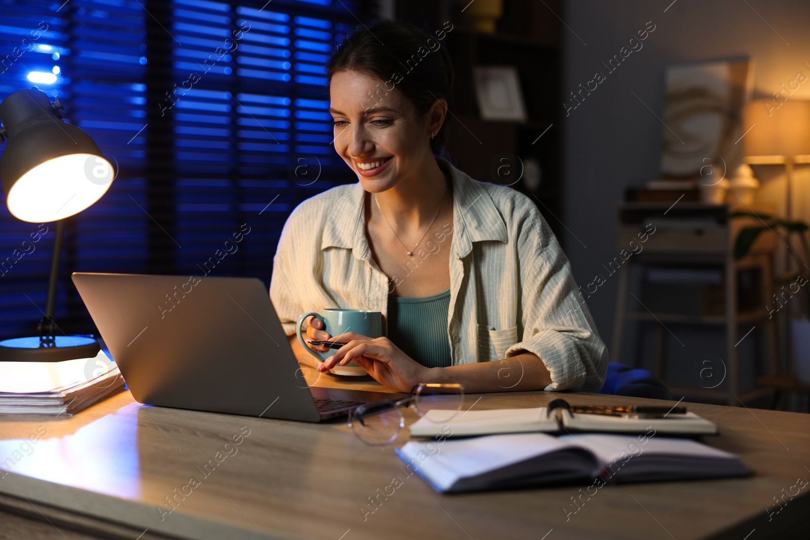 Photo of Woman with cup of coffee working on laptop at desk in home office