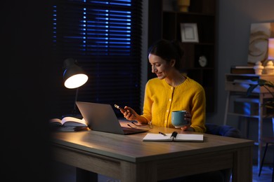 Photo of Woman with smartphone working on laptop at desk in home office