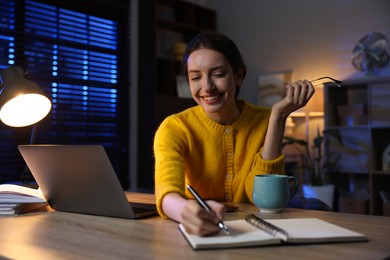 Photo of Woman taking notes while working at desk in home office