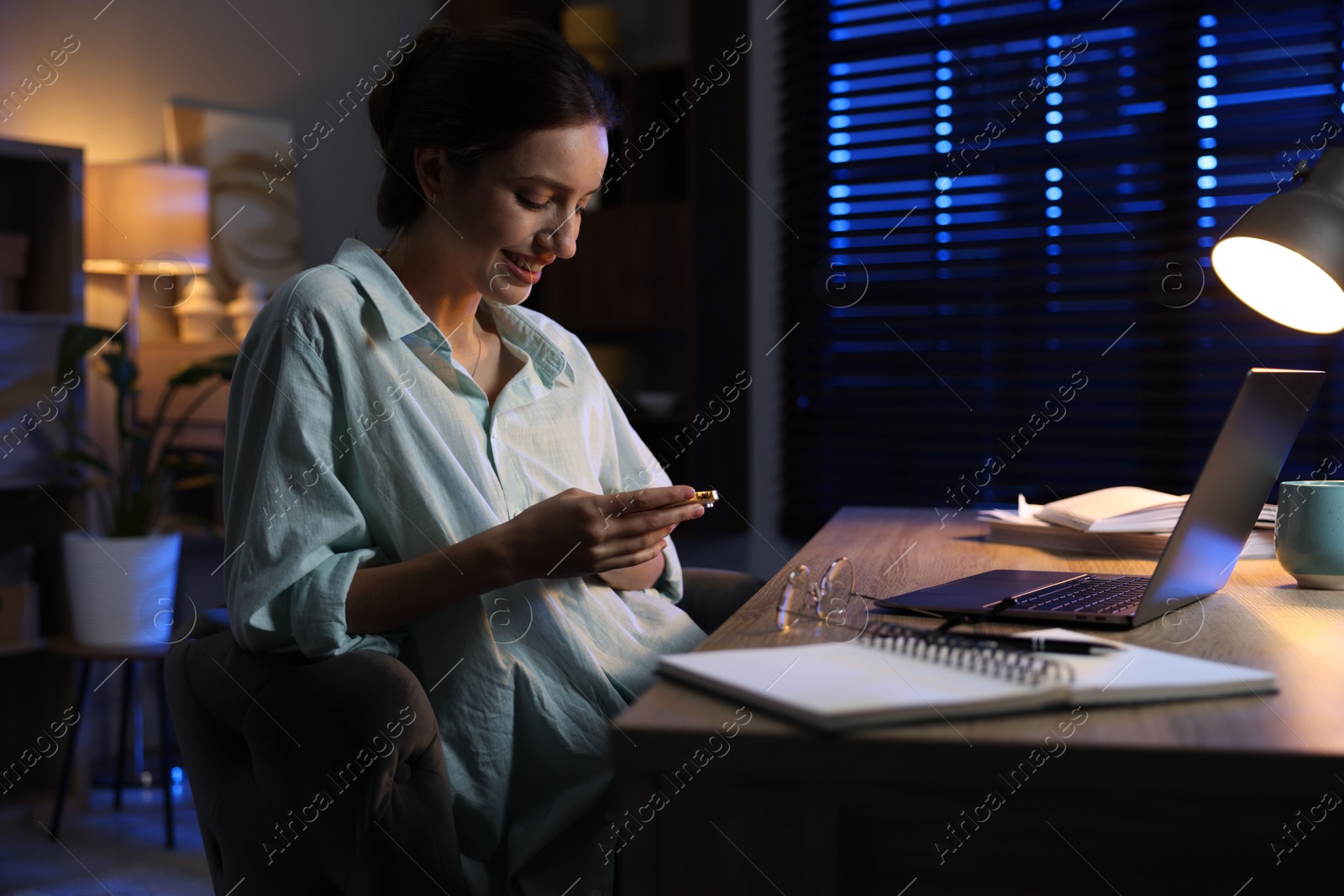 Photo of Woman with smartphone working on laptop at desk in home office