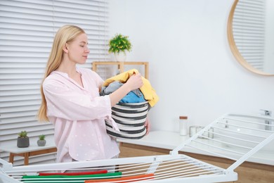 Photo of Beautiful woman hanging fresh clean laundry on drying rack at home