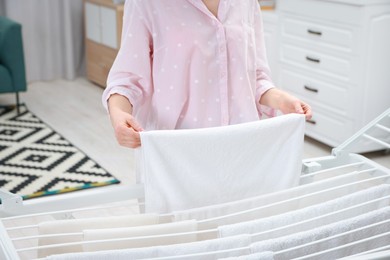 Photo of Woman hanging fresh clean laundry on drying rack at home, closeup