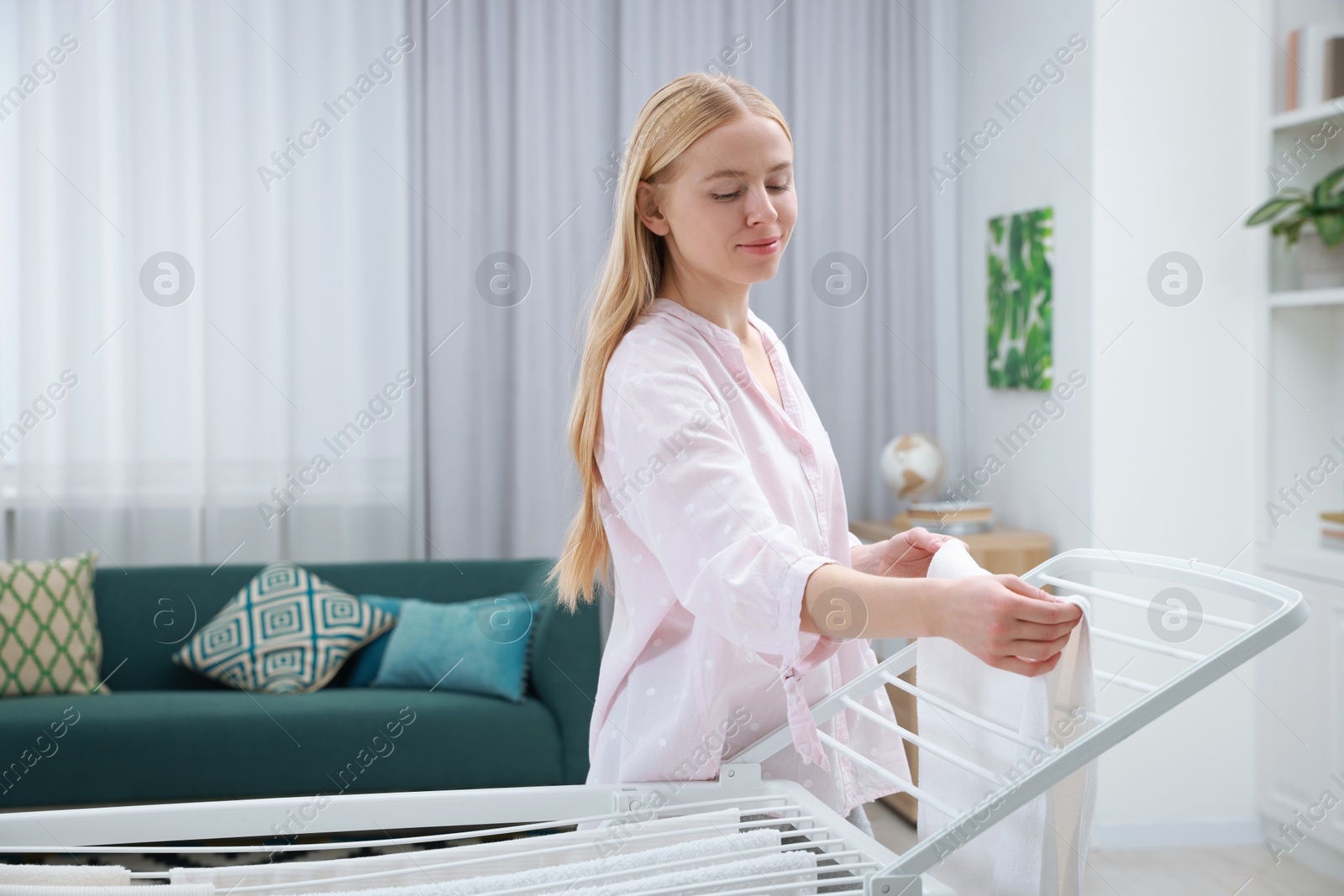 Photo of Beautiful woman hanging fresh clean laundry on drying rack at home