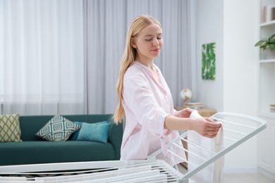 Photo of Beautiful woman hanging fresh clean laundry on drying rack at home