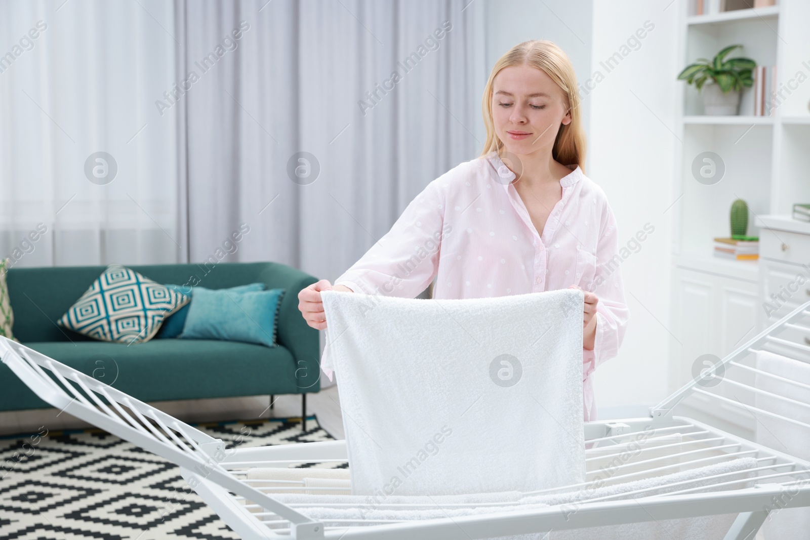 Photo of Beautiful woman hanging fresh clean laundry on drying rack at home