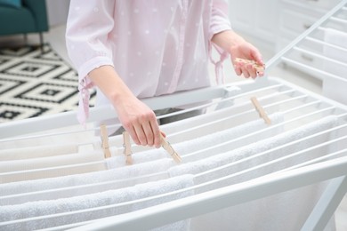 Photo of Woman hanging fresh clean laundry on drying rack at home, closeup