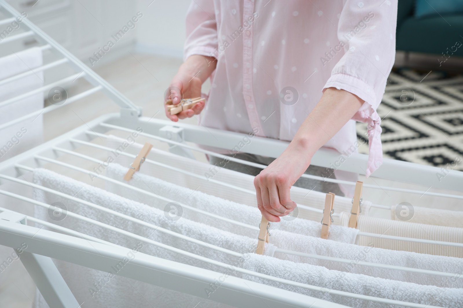 Photo of Woman hanging fresh clean laundry on drying rack at home, closeup