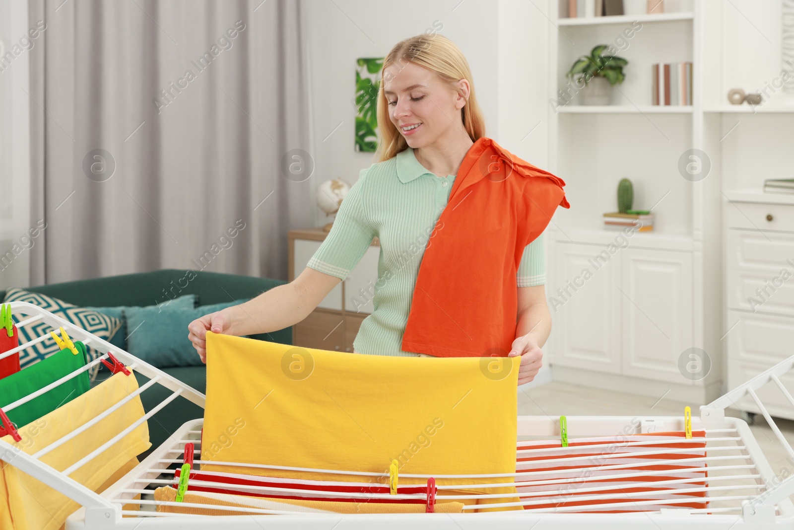 Photo of Beautiful woman hanging fresh clean laundry on drying rack at home