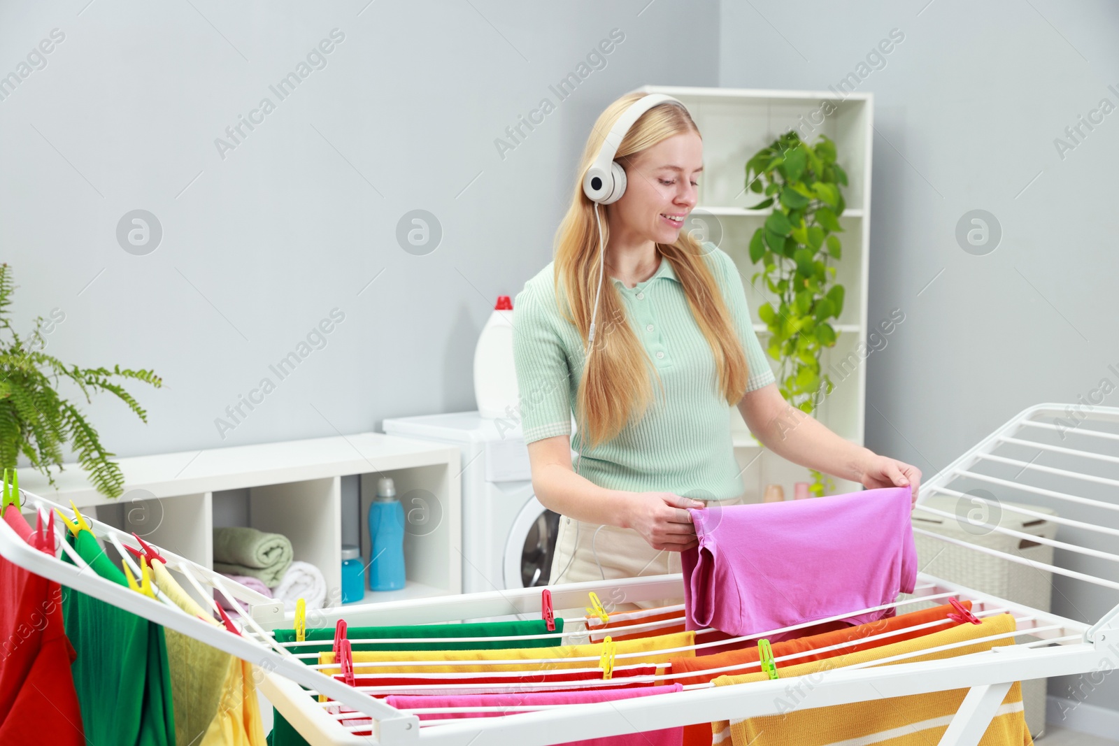 Photo of Woman listening to music while hanging fresh laundry on drying rack at home