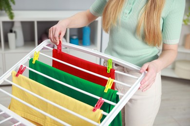 Photo of Woman hanging fresh clean laundry on drying rack at home, closeup