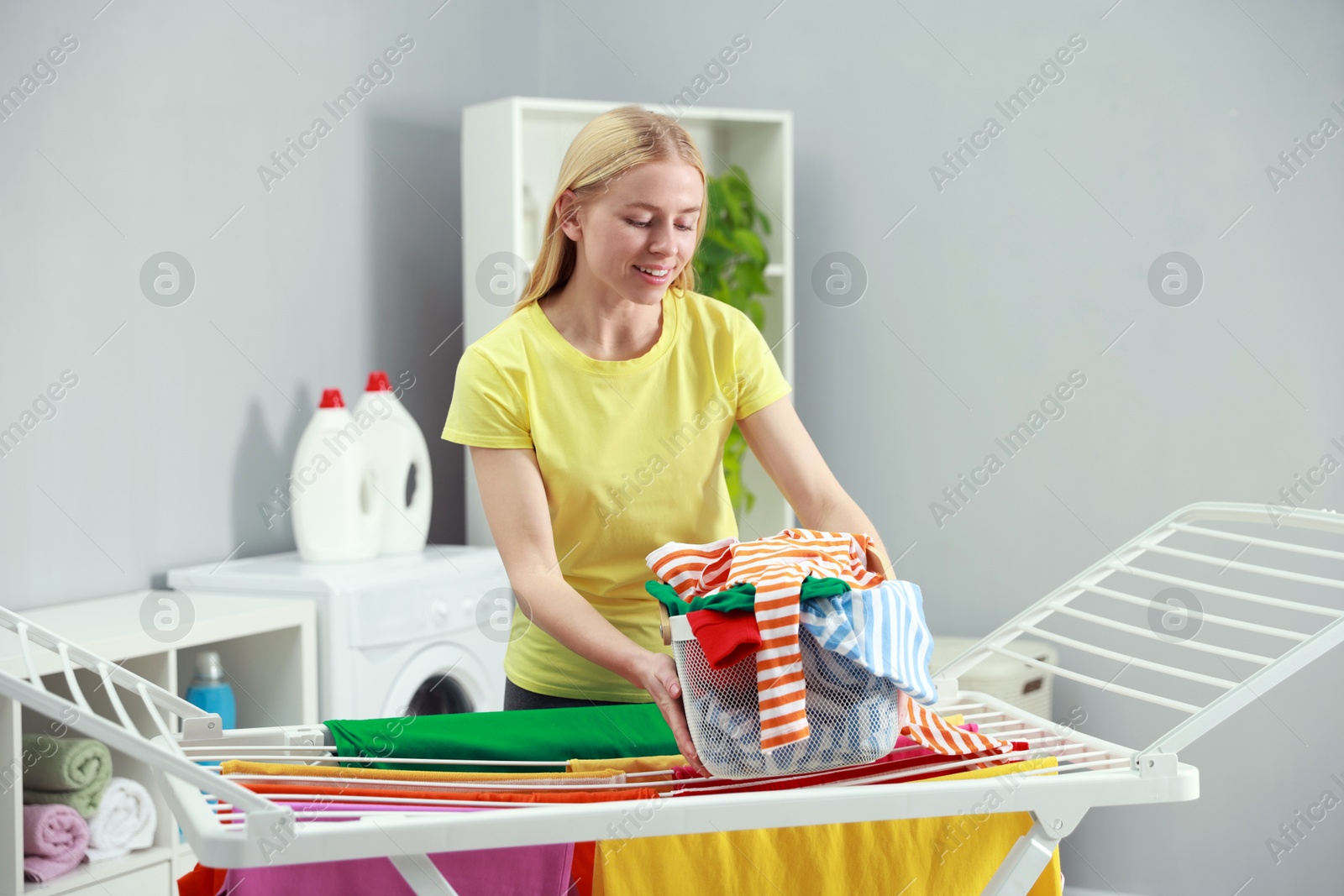 Photo of Beautiful woman hanging fresh clean laundry on drying rack at home