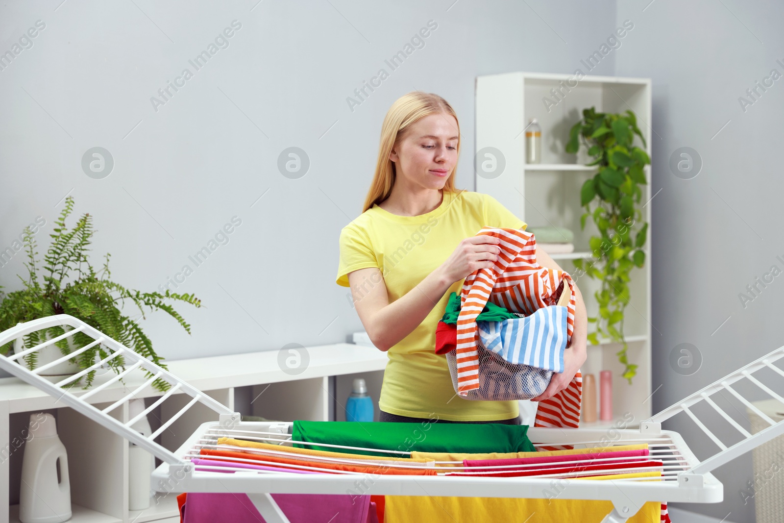 Photo of Beautiful woman hanging fresh clean laundry on drying rack at home