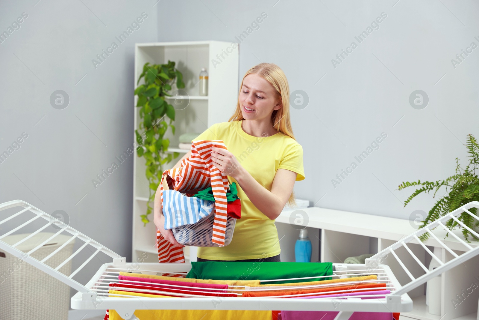 Photo of Beautiful woman hanging fresh clean laundry on drying rack at home