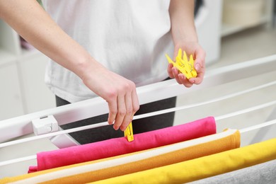 Photo of Woman hanging fresh clean laundry on drying rack at home, closeup