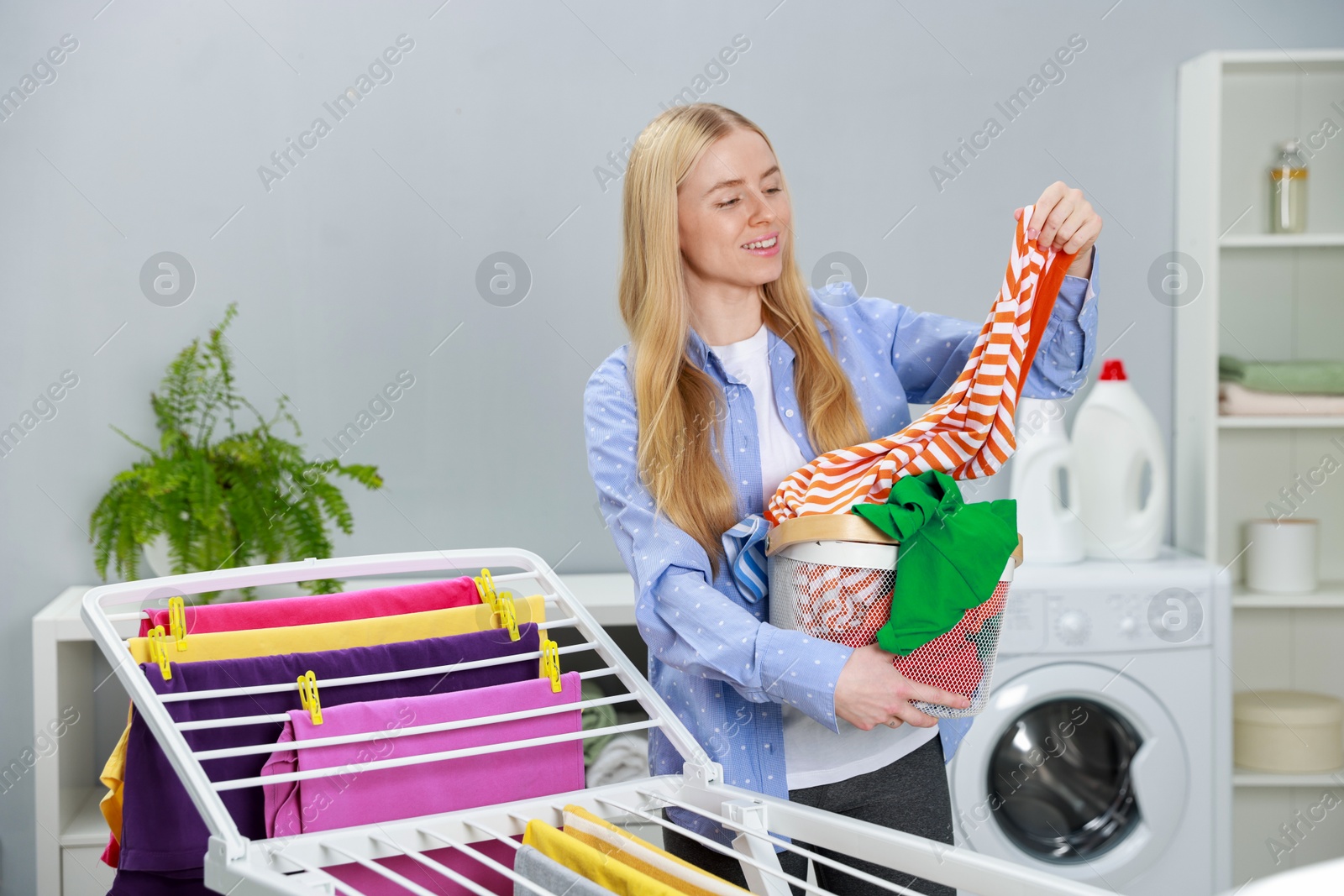 Photo of Beautiful woman hanging fresh clean laundry on drying rack at home