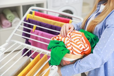 Photo of Woman hanging fresh clean laundry on drying rack at home, closeup