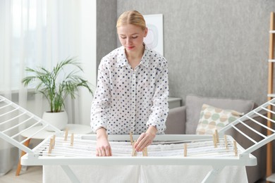 Photo of Beautiful woman hanging fresh clean laundry on drying rack at home