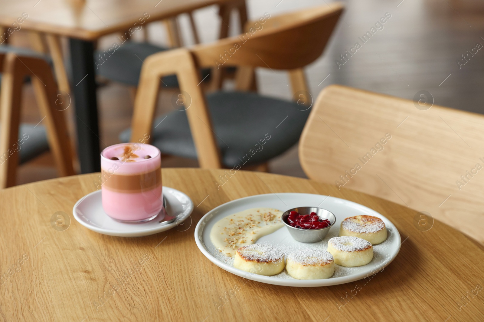 Photo of Delicious cottage cheese pancakes and pink latte served on wooden table indoors