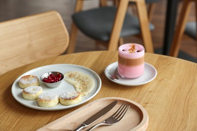 Photo of Delicious cottage cheese pancakes and pink latte served on wooden table indoors