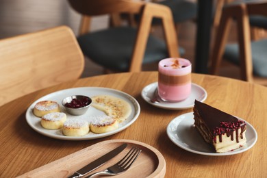 Photo of Delicious cottage cheese pancakes, cake and coffee served on wooden table in cafe