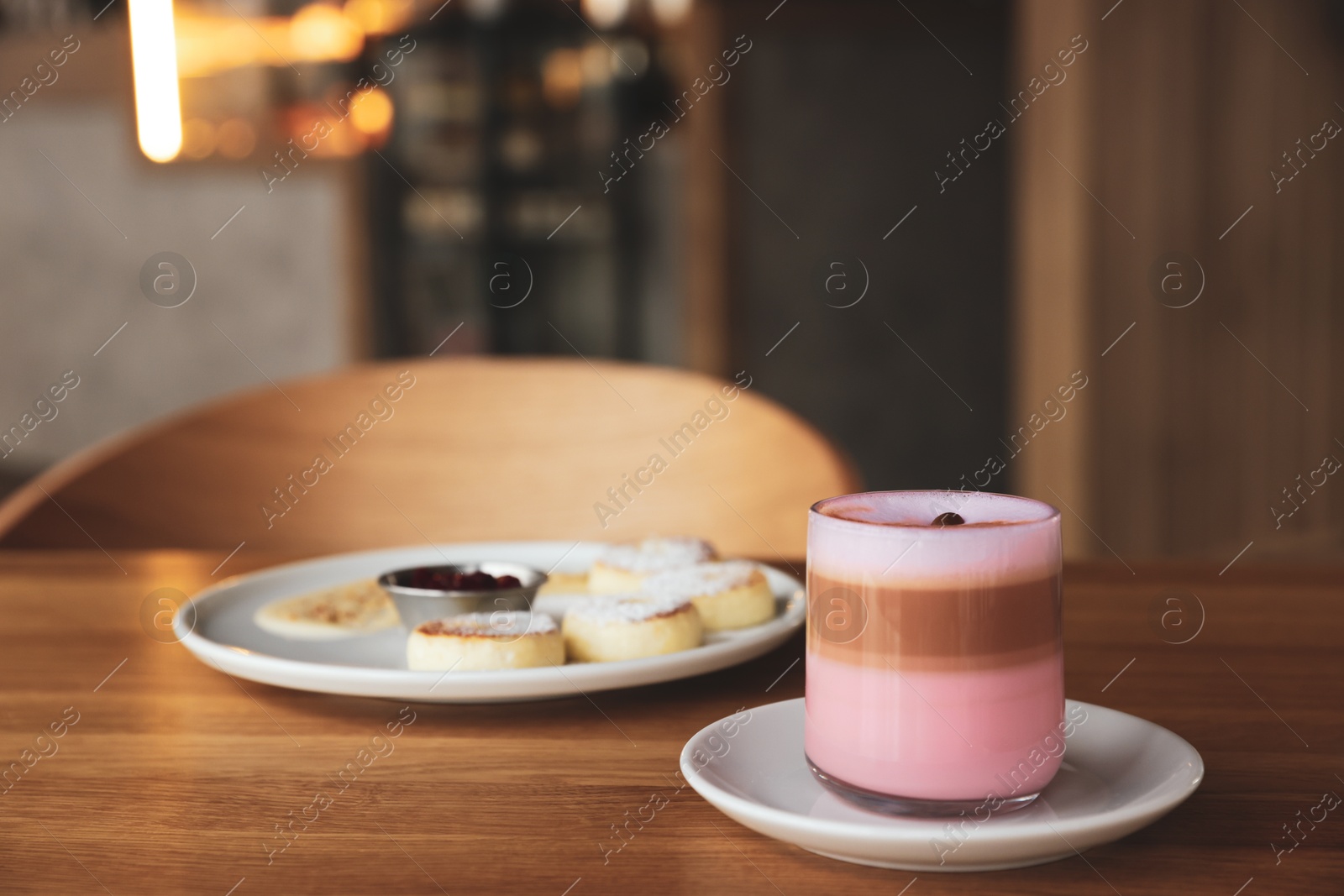 Photo of Delicious cottage cheese pancakes and pink latte served on wooden table indoors