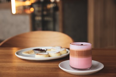 Photo of Delicious cottage cheese pancakes and pink latte served on wooden table indoors