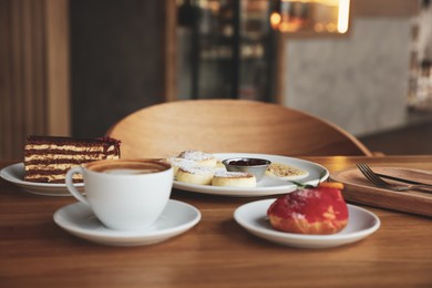 Photo of Aromatic coffee and delicious desserts served on wooden table in cafe