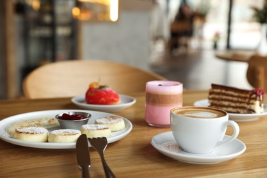 Photo of Delicious cottage cheese pancakes, desserts and aromatic coffee served on wooden table in cafe