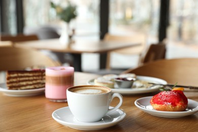 Photo of Aromatic coffee and delicious desserts served on wooden table in cafe