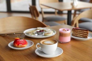 Photo of Aromatic coffee and delicious desserts served on wooden table in cafe