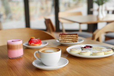 Photo of Delicious cottage cheese pancakes, desserts and aromatic coffee served on wooden table in cafe