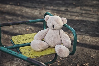 Photo of Lost white teddy bear on merry-go-round outdoors, closeup