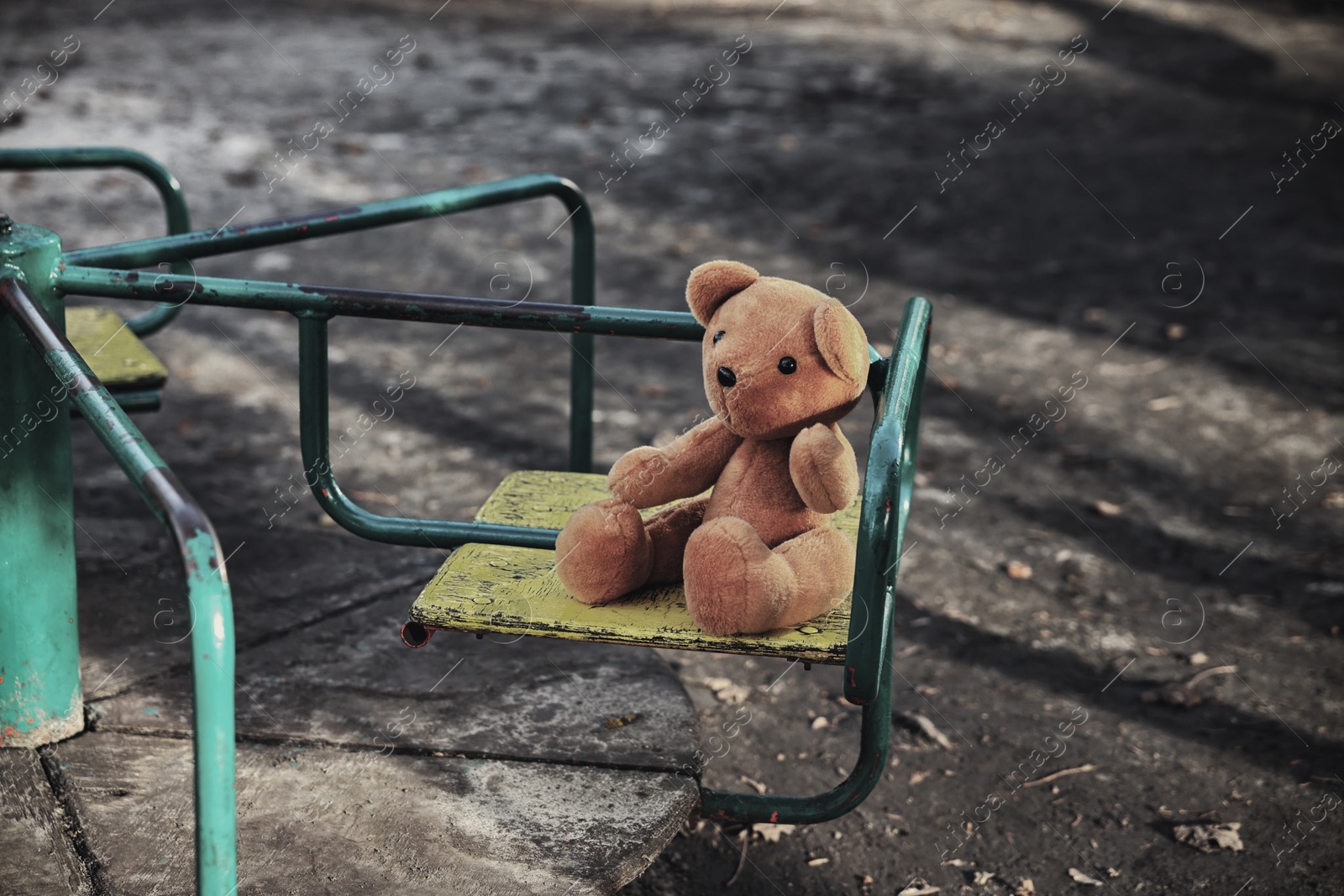 Photo of Lost brown teddy bear on merry-go-round outdoors, closeup