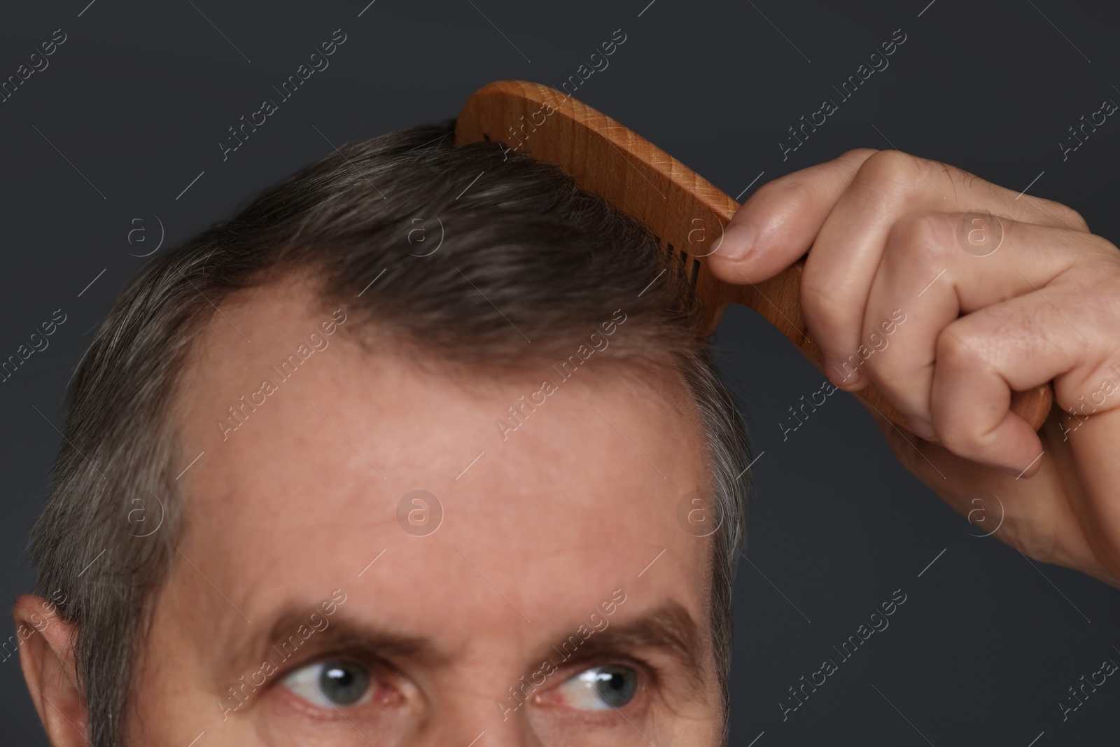 Photo of Man combing his hair on dark grey background, closeup