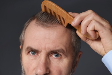 Photo of Man combing his hair on dark grey background, closeup