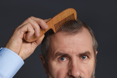 Photo of Man combing his hair on dark grey background, closeup