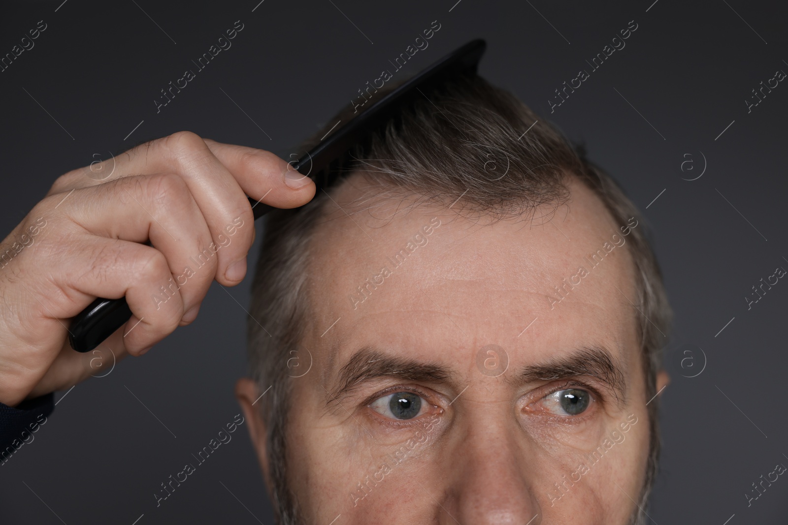 Photo of Man combing his hair on dark grey background, closeup