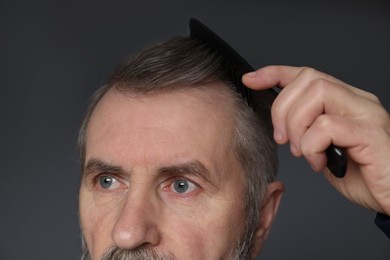 Photo of Man combing his hair on dark grey background, closeup