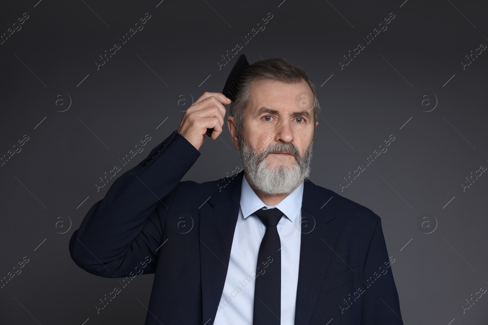 Photo of Handsome man combing his hair on dark grey background