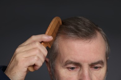 Photo of Man combing his hair on dark grey background, closeup