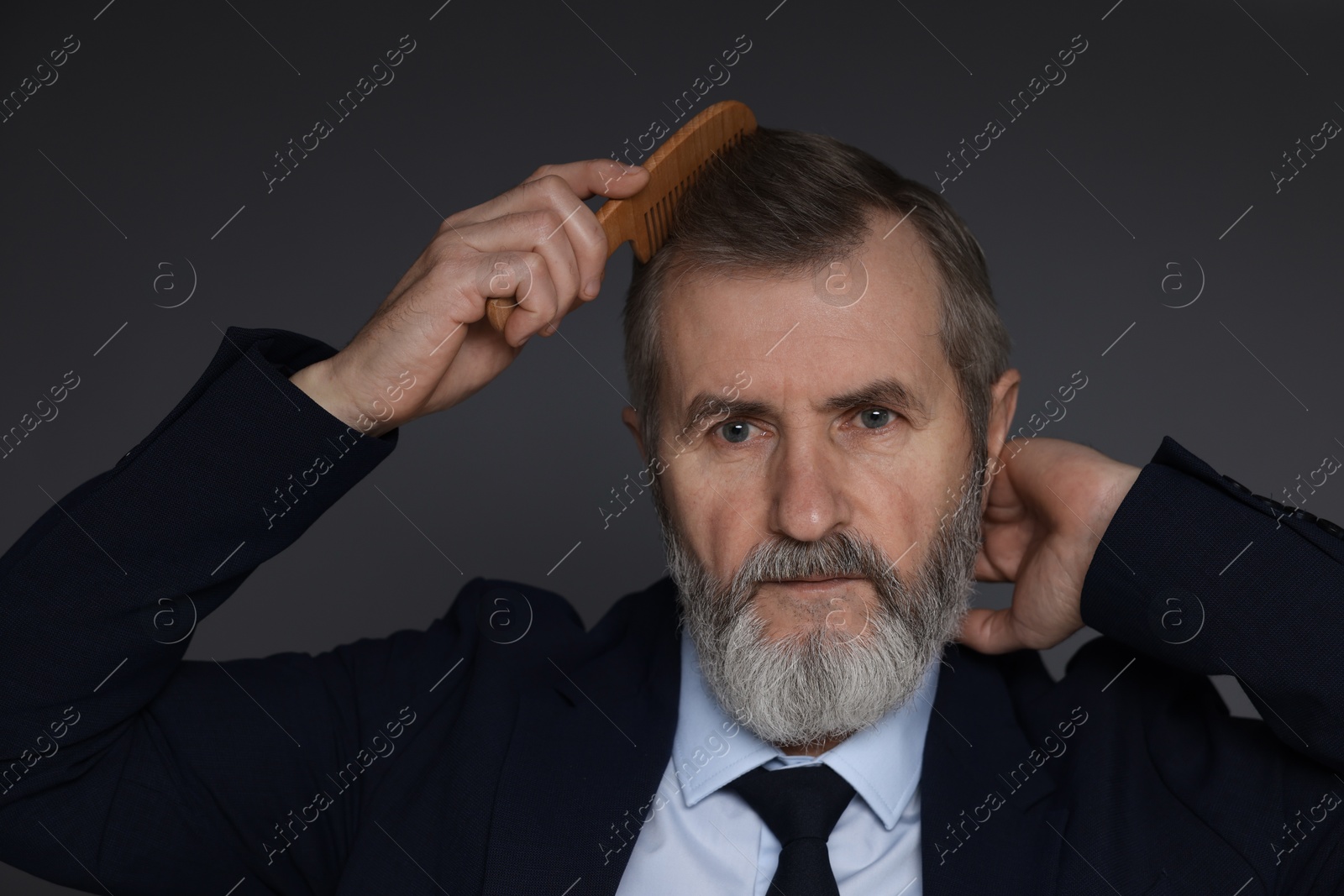 Photo of Handsome man combing his hair on dark grey background