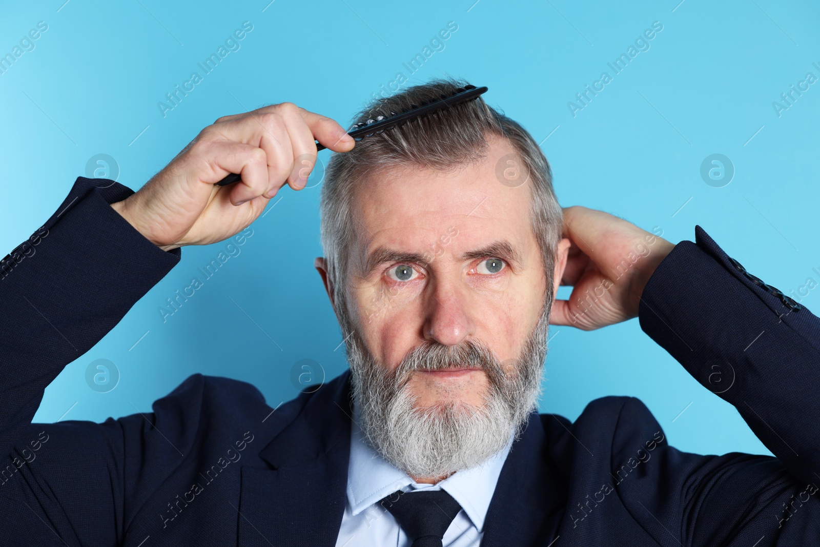 Photo of Handsome man combing his hair on light blue background