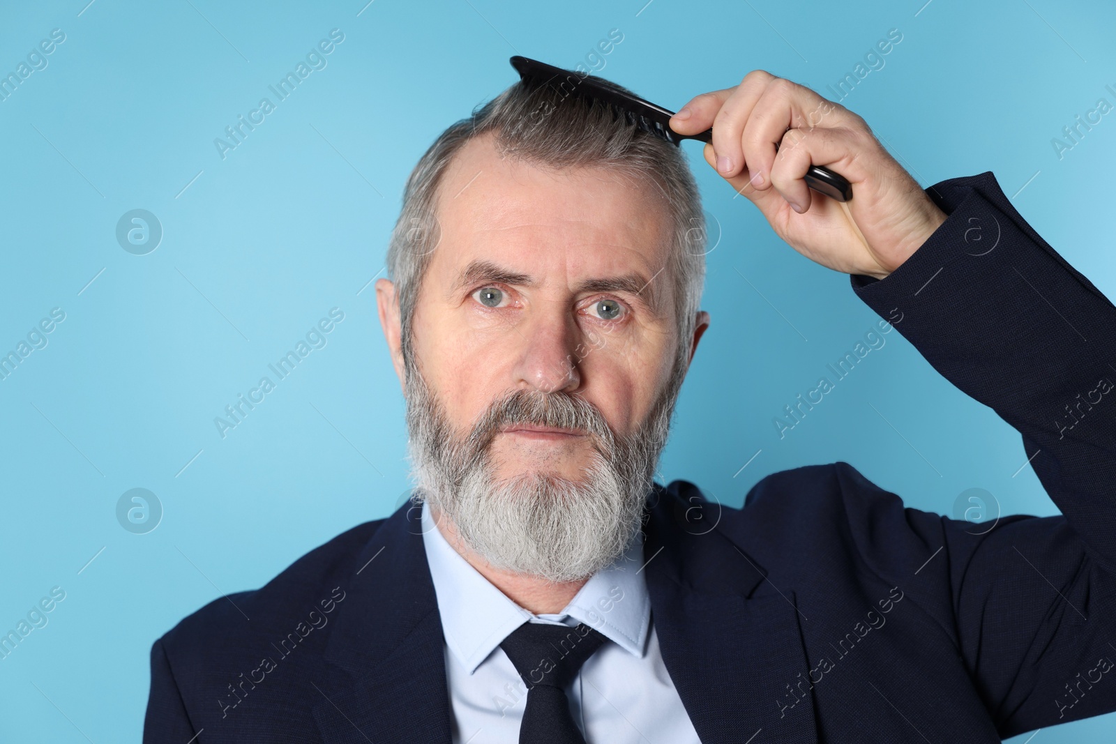 Photo of Handsome man combing his hair on light blue background