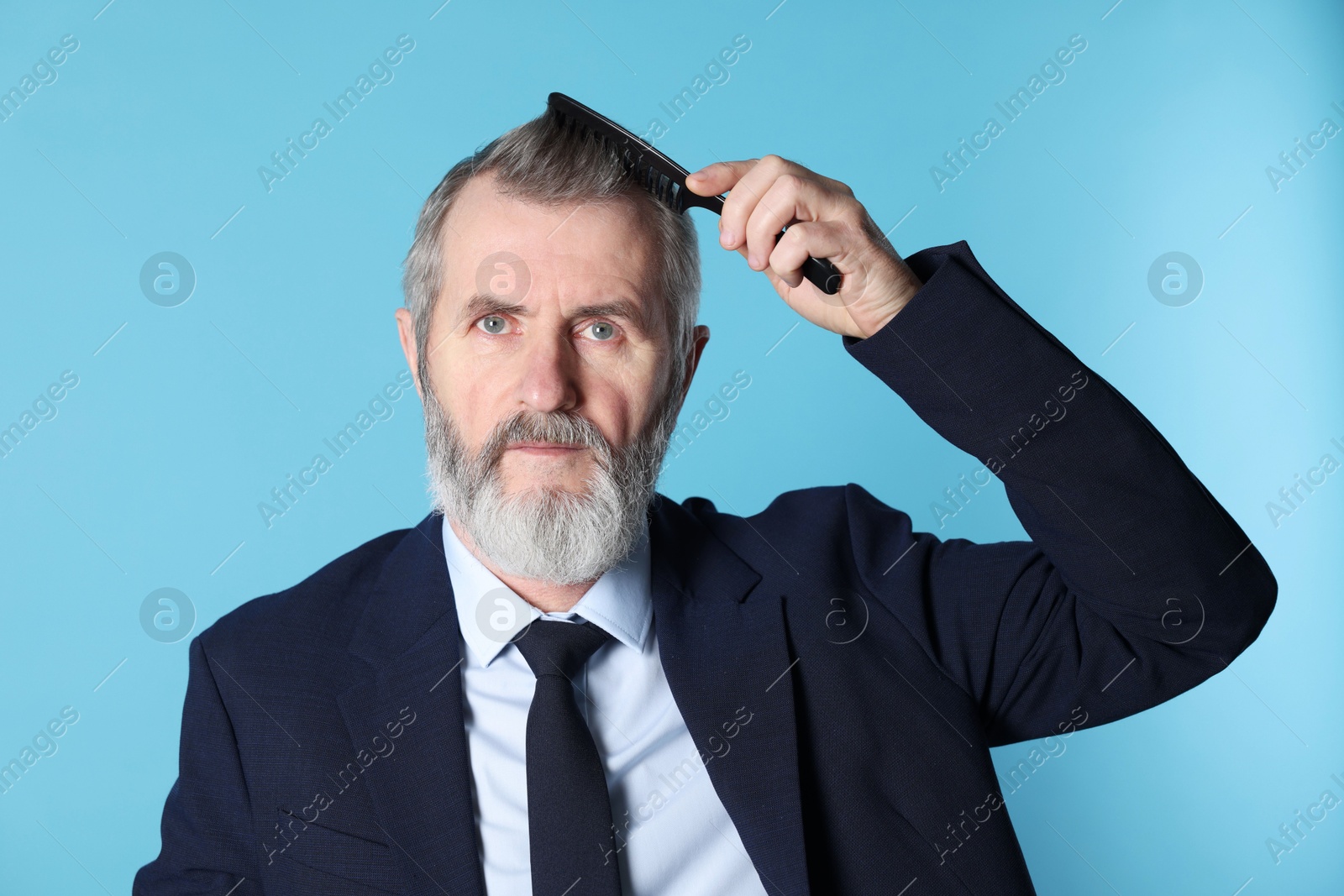 Photo of Handsome man combing his hair on light blue background