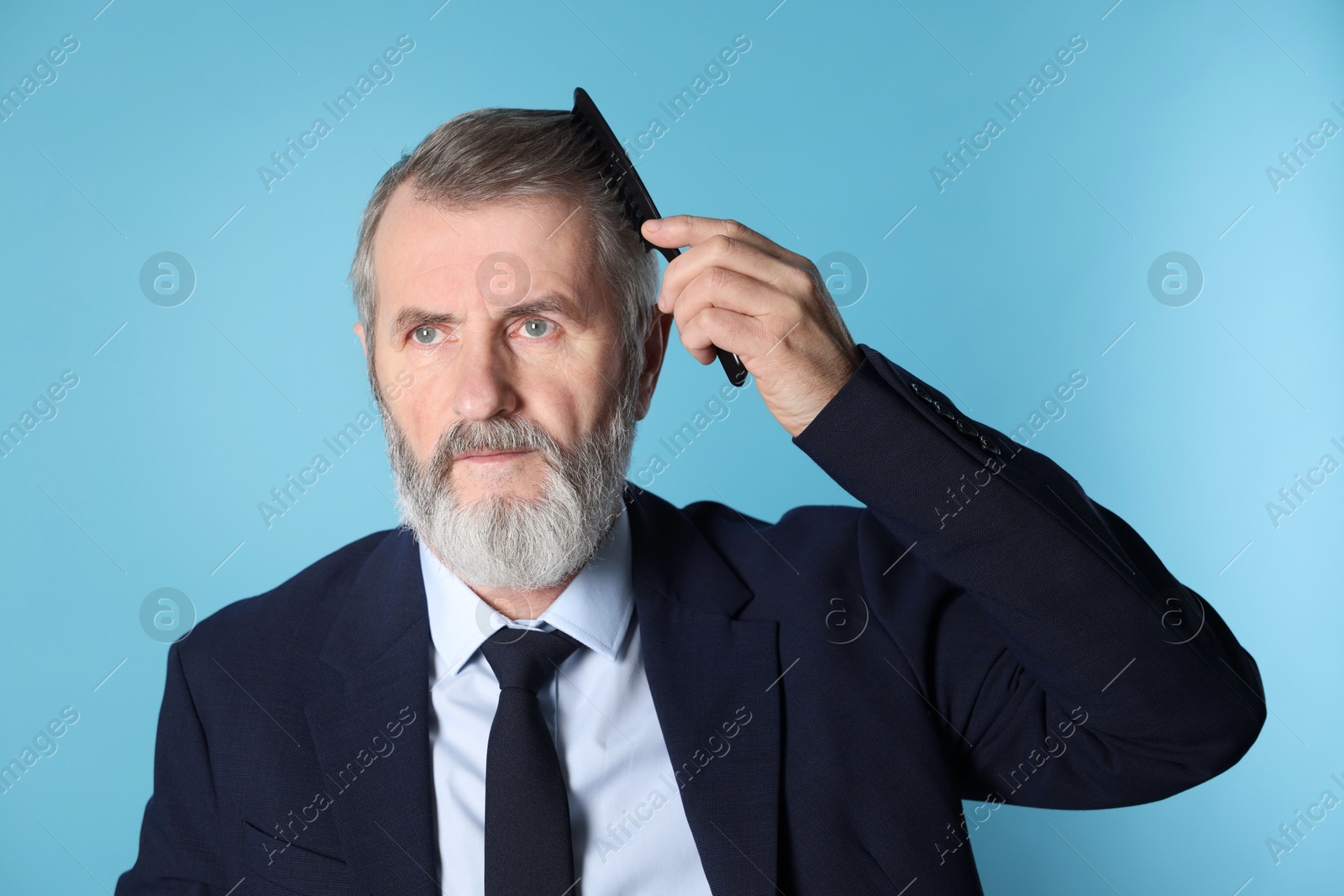 Photo of Handsome man combing his hair on light blue background