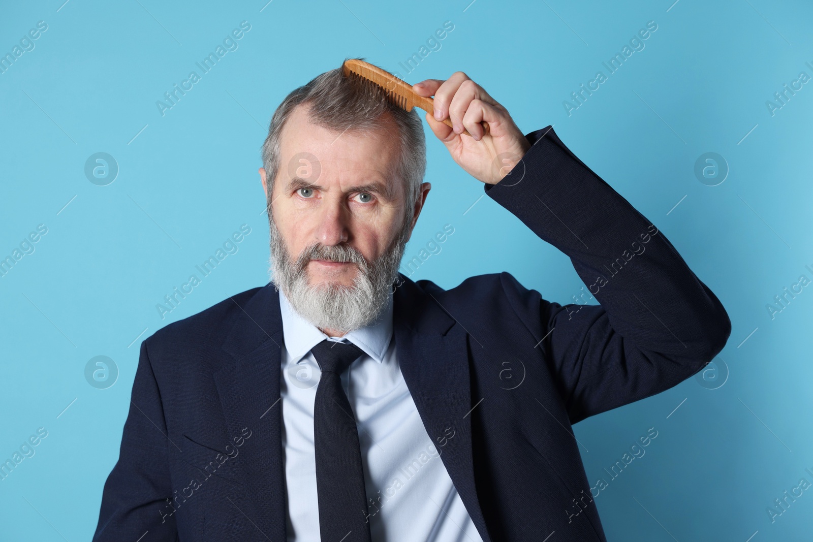 Photo of Handsome man combing his hair on light blue background