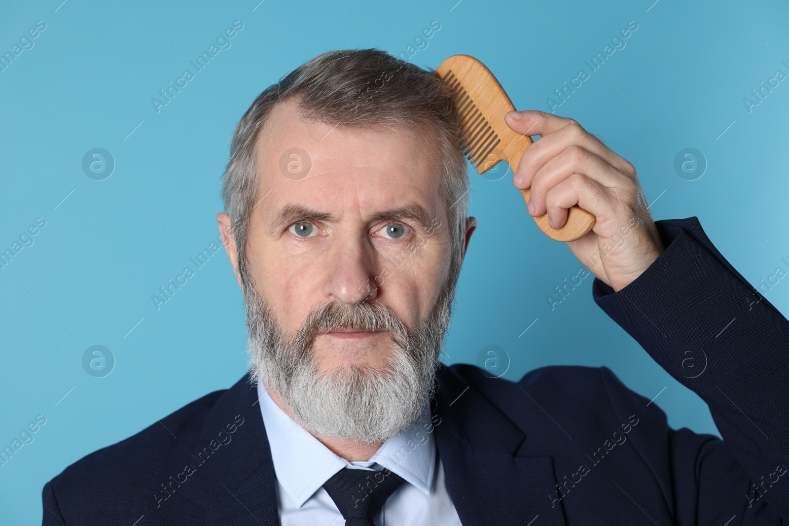 Photo of Handsome man combing his hair on light blue background