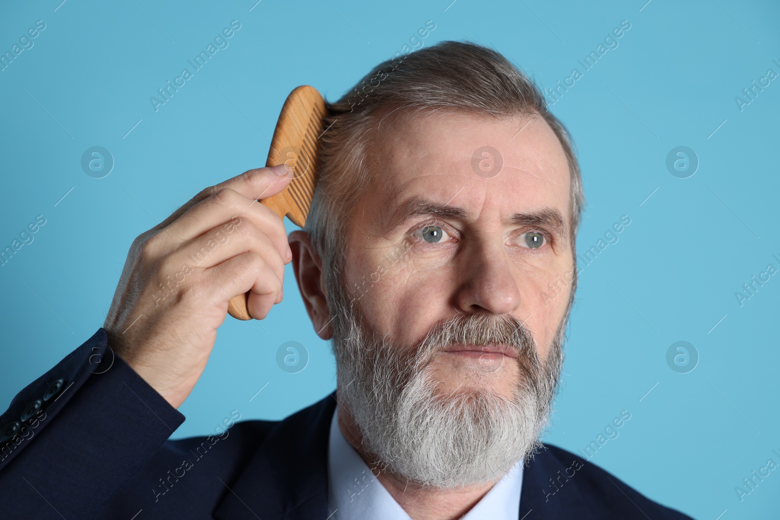 Photo of Handsome man combing his hair on light blue background, closeup