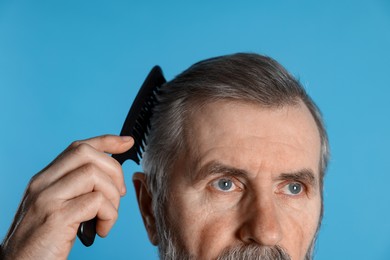 Photo of Man combing his hair on light blue background, closeup